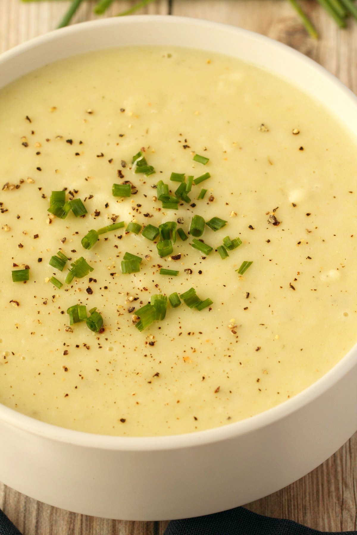 Vegan potato leek soup topped with chopped chives in a white bowl.