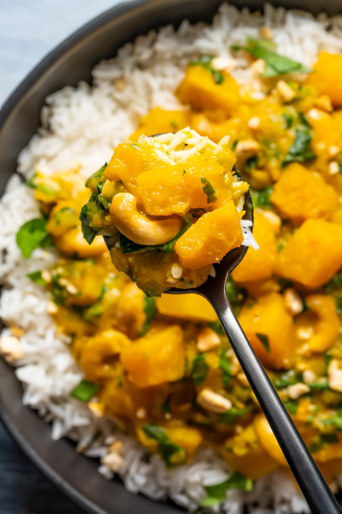 Thai pumpkin curry with rice in a black bowl with a spoon.