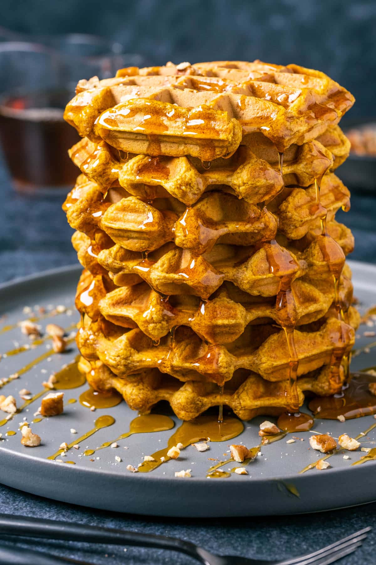 Vegan pumpkin waffles with syrup and chopped pecans on a gray plate. 