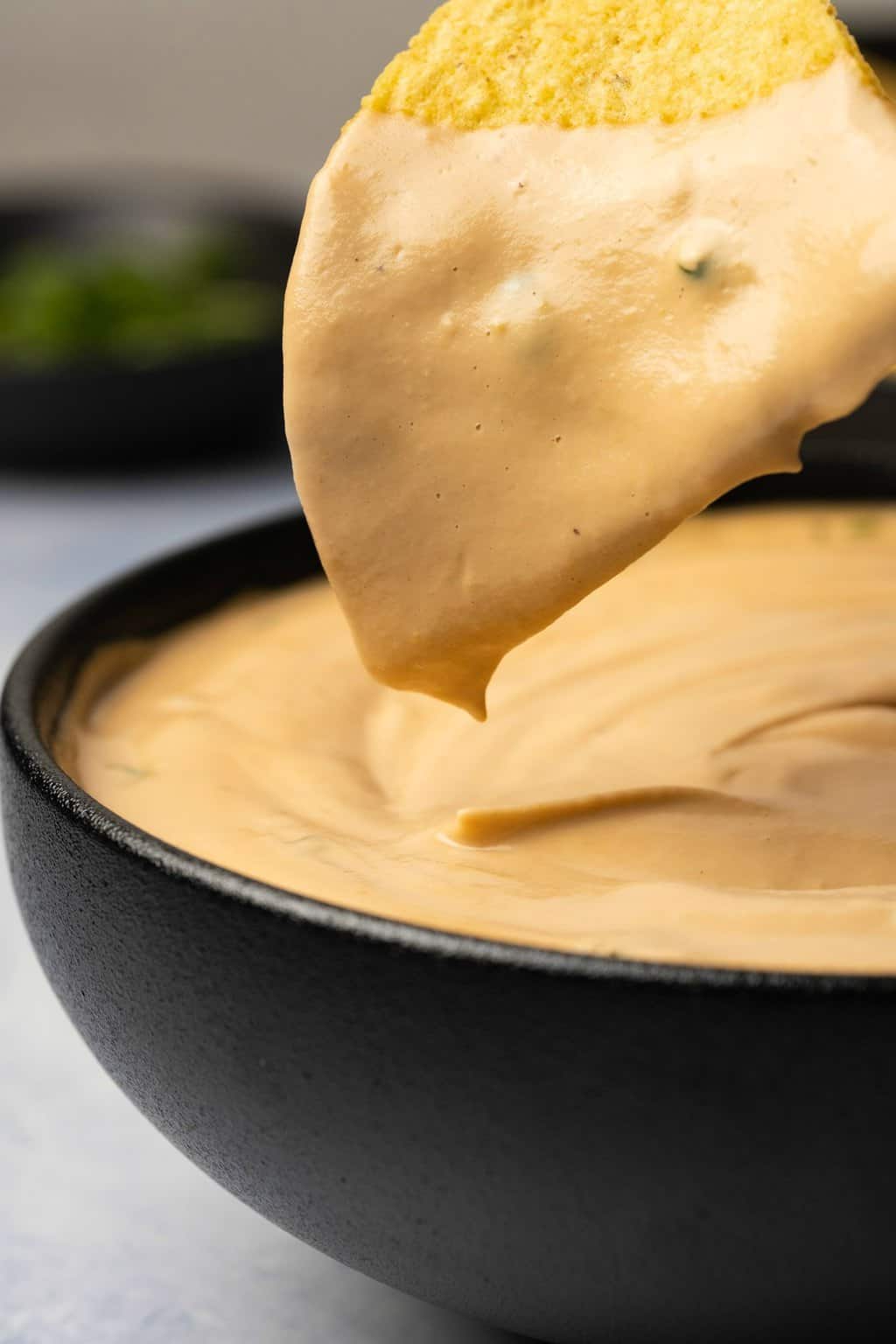 Tortilla chip dipping into a bowl of queso. 