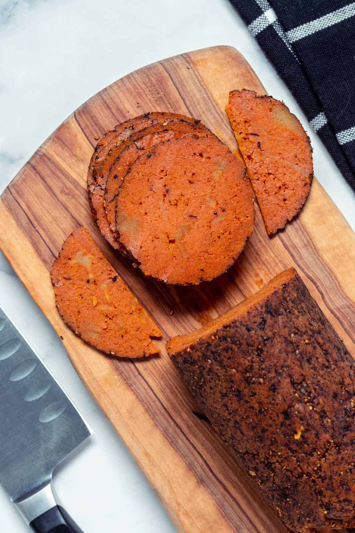 Slices of vegan salami stacked up on a wooden board.