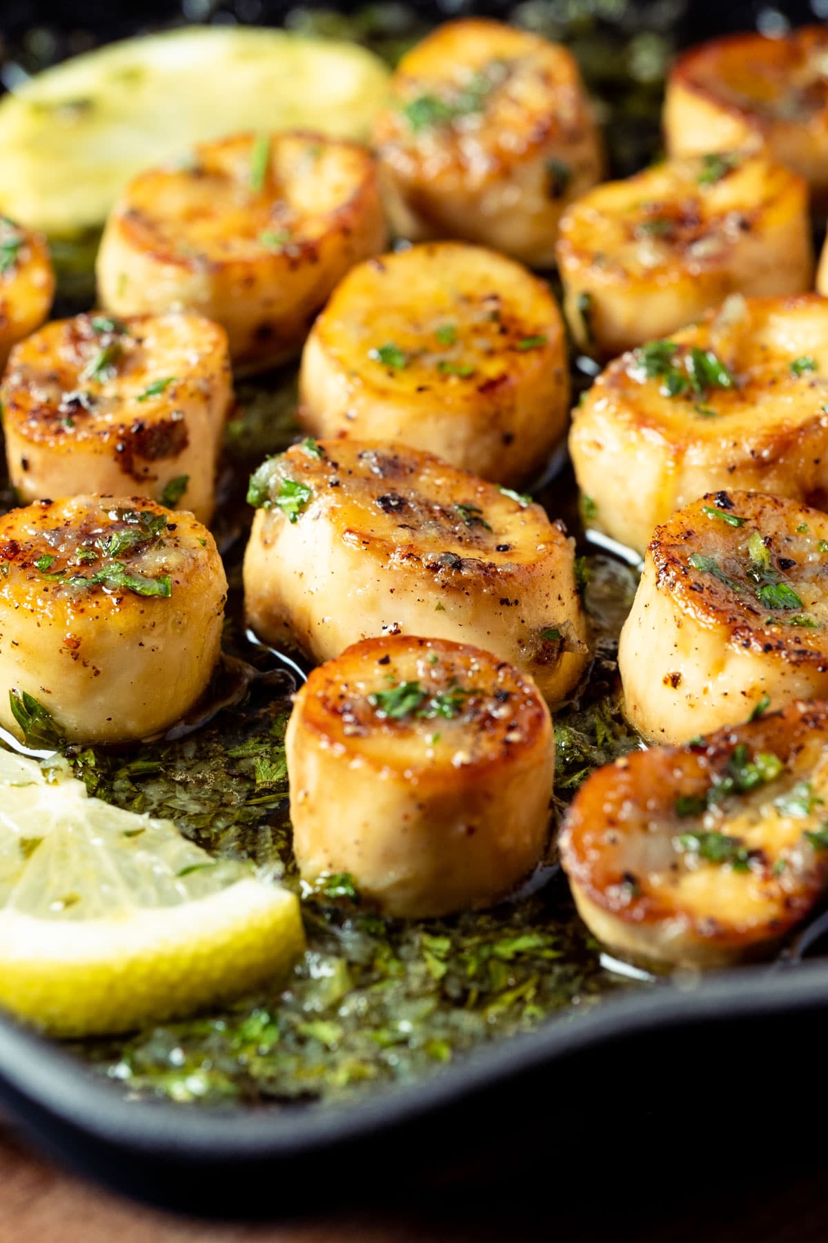 Vegan scallops with lemon slices and parsley in a frying pan.