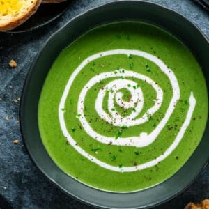 Vegan spinach soup in a black bowl with a swirl of coconut cream on top.