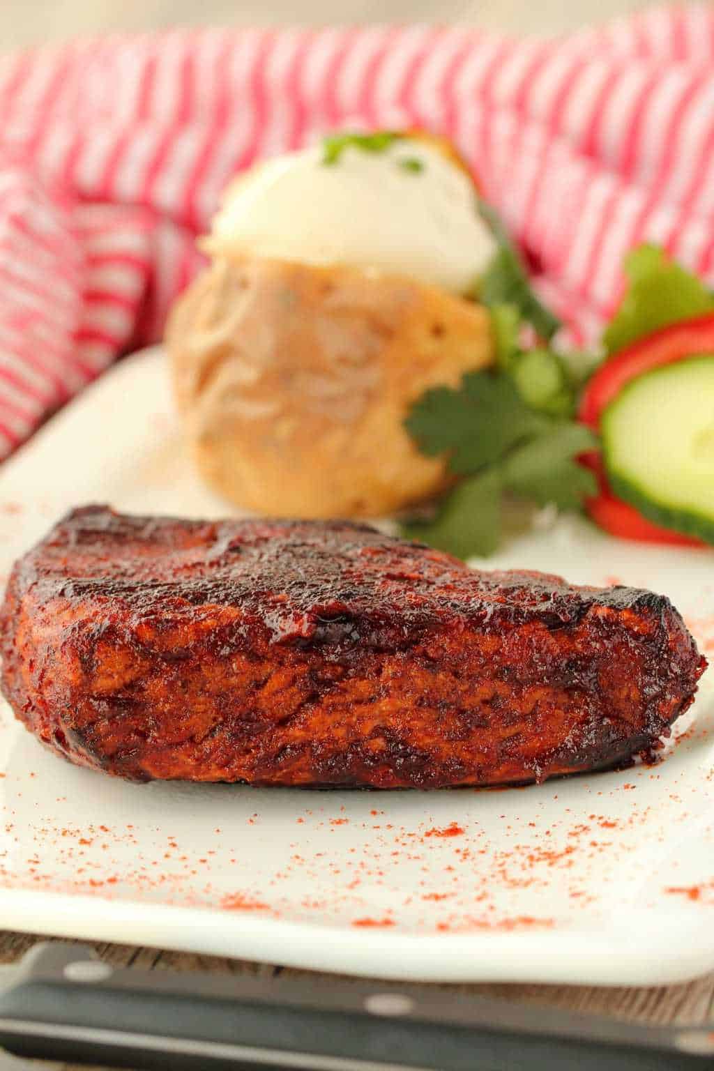 Vegan Steak on a white plate with a baked potato and salad garnish. 