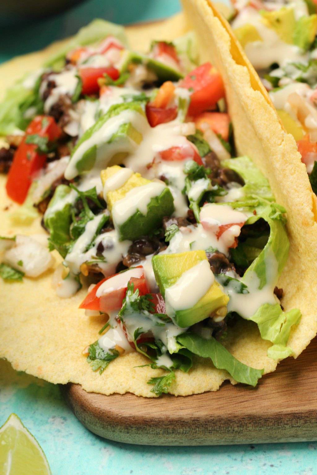 Vegan tacos stuffed with black beans, vegan taco meat, pico de gallo, avocado and tahini sauce on a wooden board. 