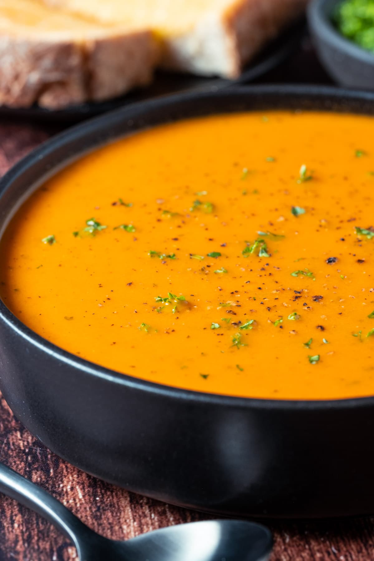 Vegan tomato soup topped with fresh chopped parsley in a black bowl.