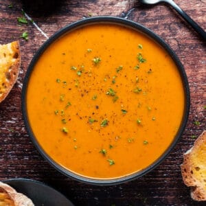 Vegan tomato soup topped with fresh chopped parsley in a black bowl.