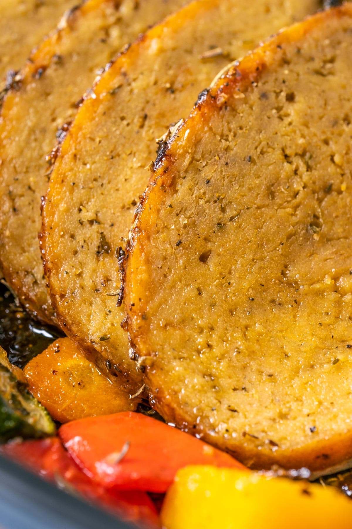 Slices of vegan turkey roast in a roasting pan with vegetables.