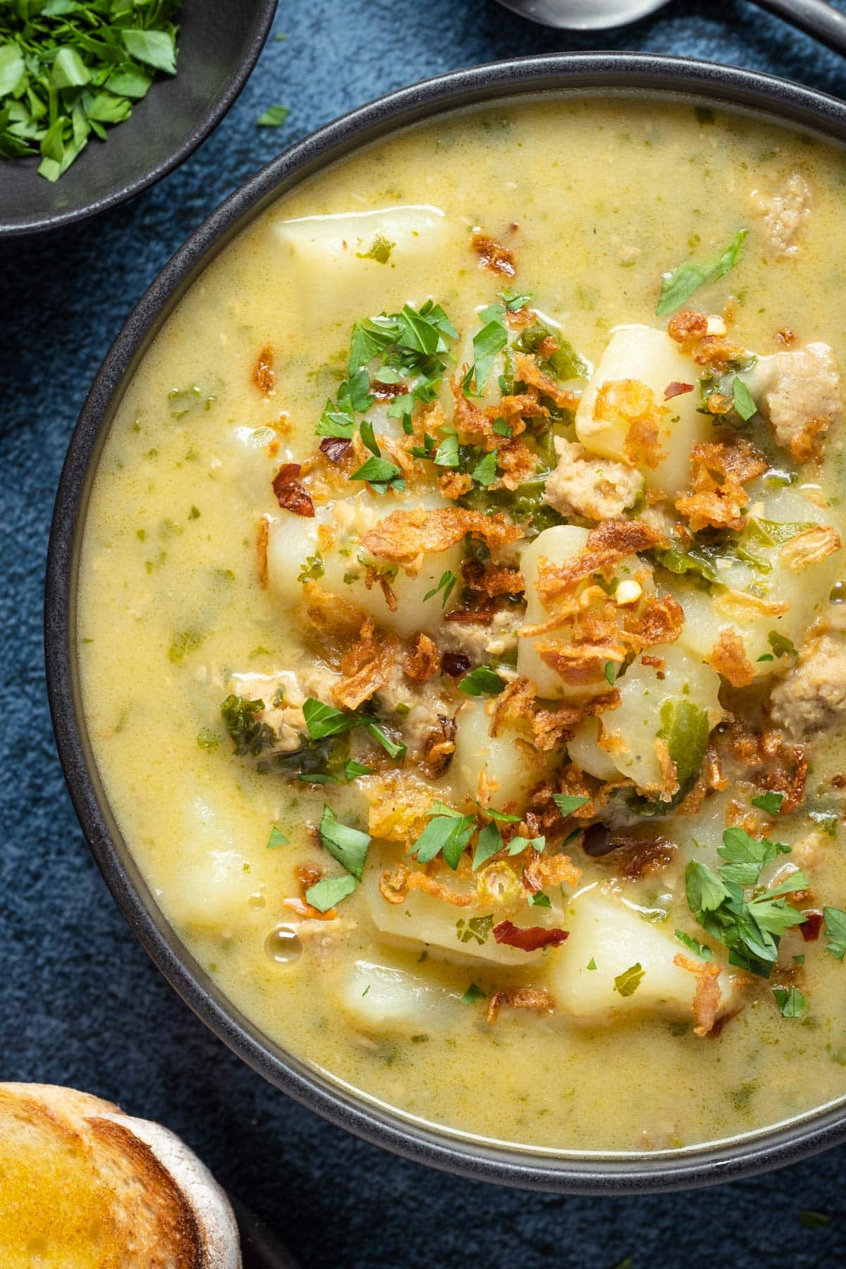 Vegan zuppa toscana topped with crispy fried onions and parsley in a black bowl.