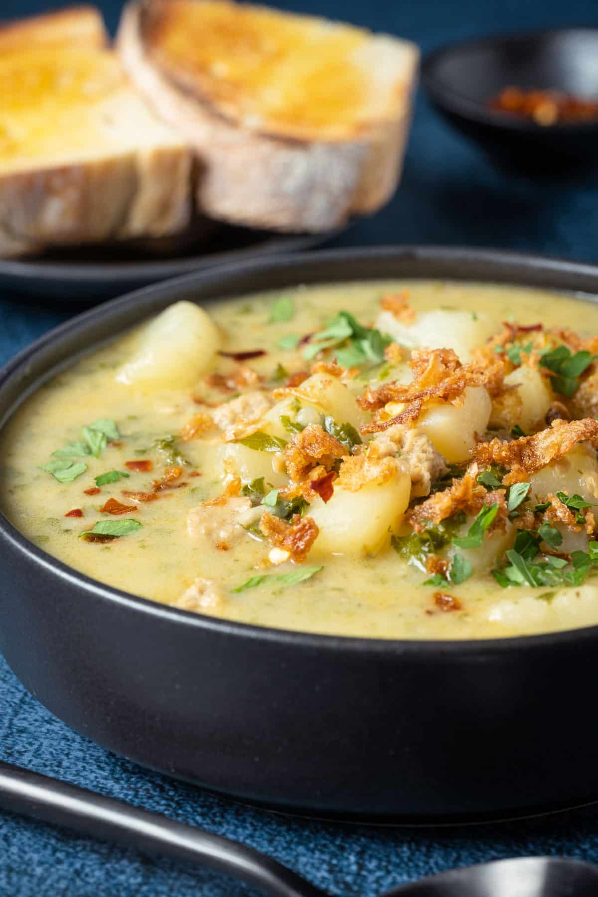 Vegan zuppa toscana topped with crispy fried onions and parsley in a black bowl.