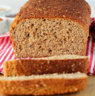 Slice loaf of whole wheat bread on a wooden board.