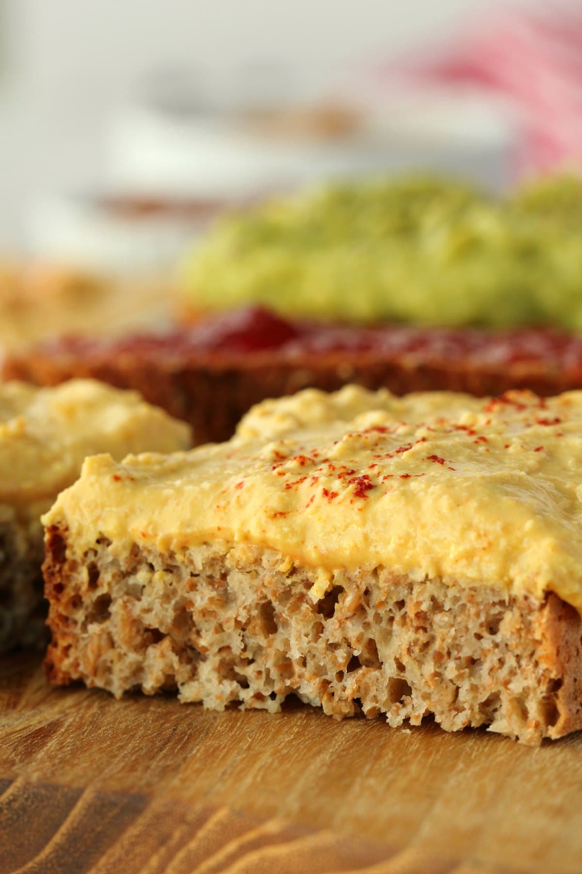 A slice of whole wheat bread topped with hummus and sliced in half. 